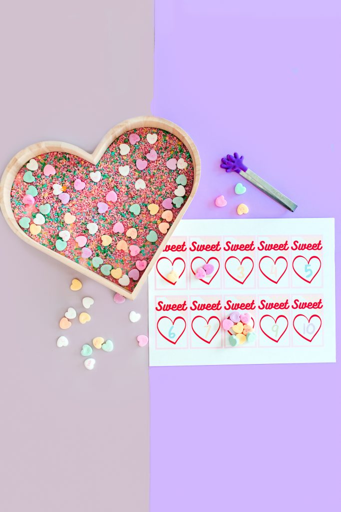 Sensory bin for hands on Valentine math activity. Preschool and Kindergarten. Conversation hearts for counting, grouping, and addition. Free printable. 