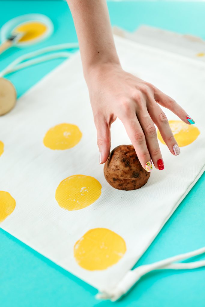 Using paint and a potato stamp to design a DIY emoji backpack.