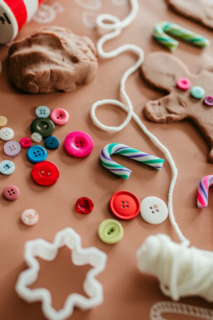 Homemade gingerbread playdough play kit including cookie cutters, buttons, candy, and yarn. 