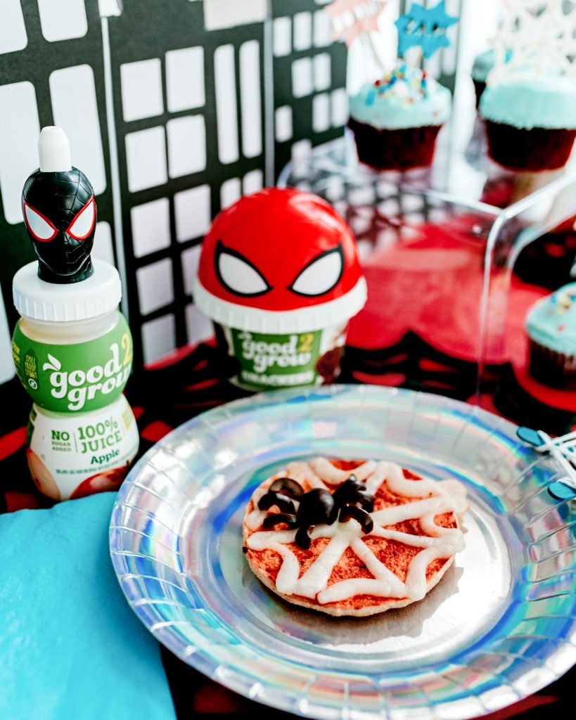 Mini English muffin pizzas decorated with string cheese webs and black olive spiders for Spiderman themed kids party.