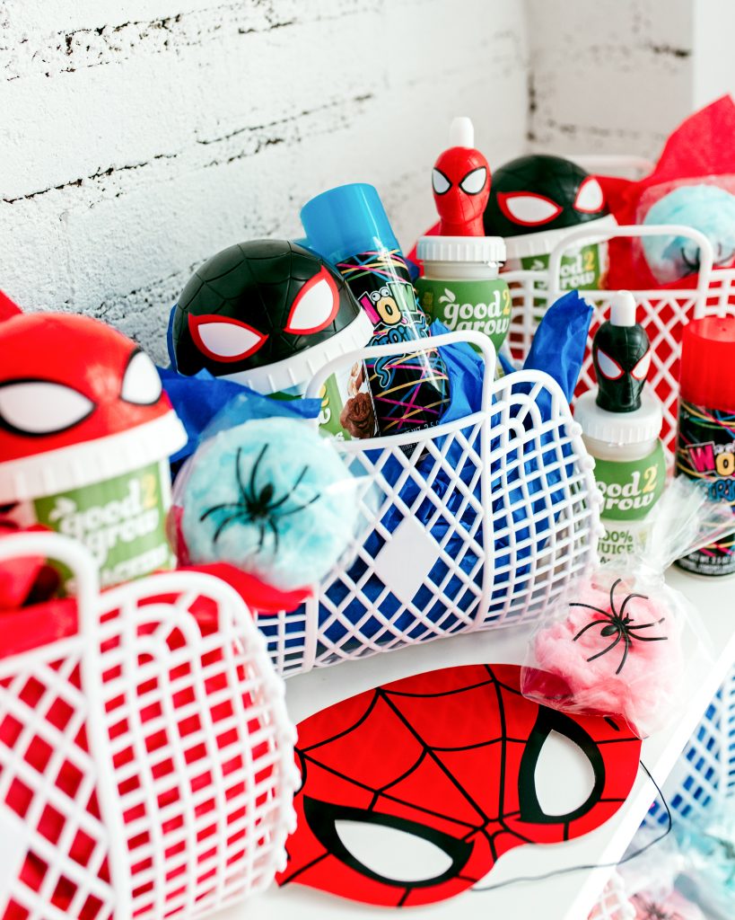 Spiderman party favor basket filled with themed drinks, snack cups, mask, cotton candy ‘webs,’ and silly string.