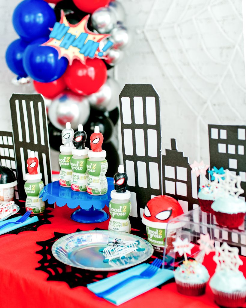Close-up of a superhero party tablescape featuring spider web placemats, iridescent plates, and Spider-Man-themed snack cups.