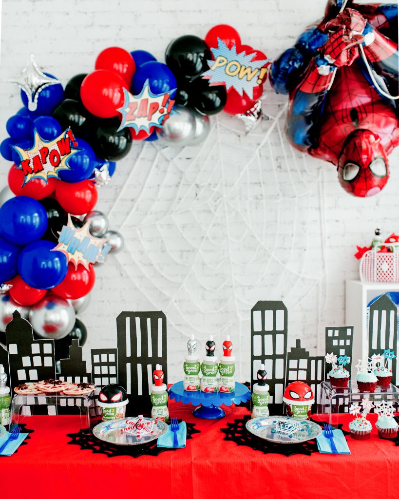 Spiderman themed party table with DIY cityscape backdrop, superhero party wall decor with large balloon garland and oversized Spider-Man balloon swinging into the scene.