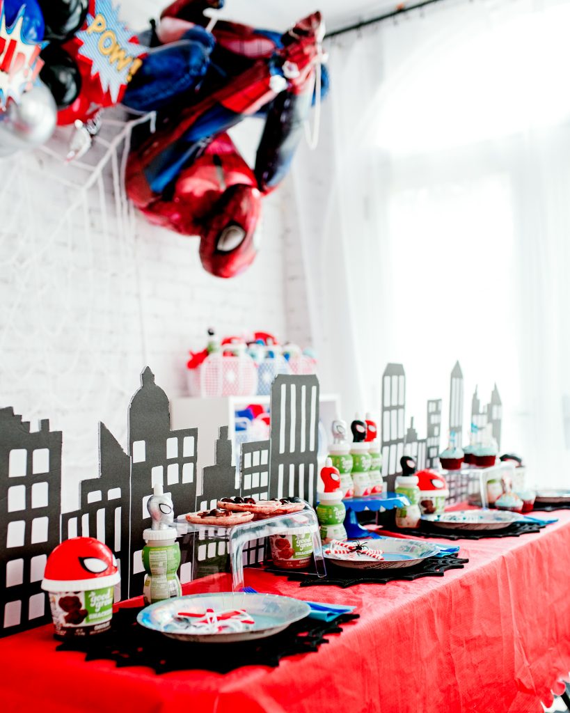 DIY city skyline made from black foam board displayed behind a colorful Spiderman birthday table setup.